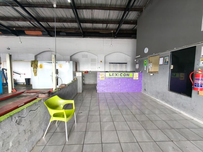 Industrial utility space featuring a service counter, tiled flooring, and exposed roof structure, currently utilized as a vehicle inspection or workshop area.