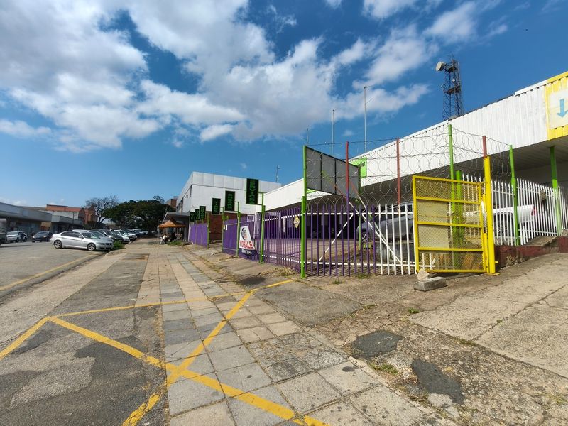 Street-level view of a commercial property featuring security fencing, razor wire, and a paved sidewalk area.