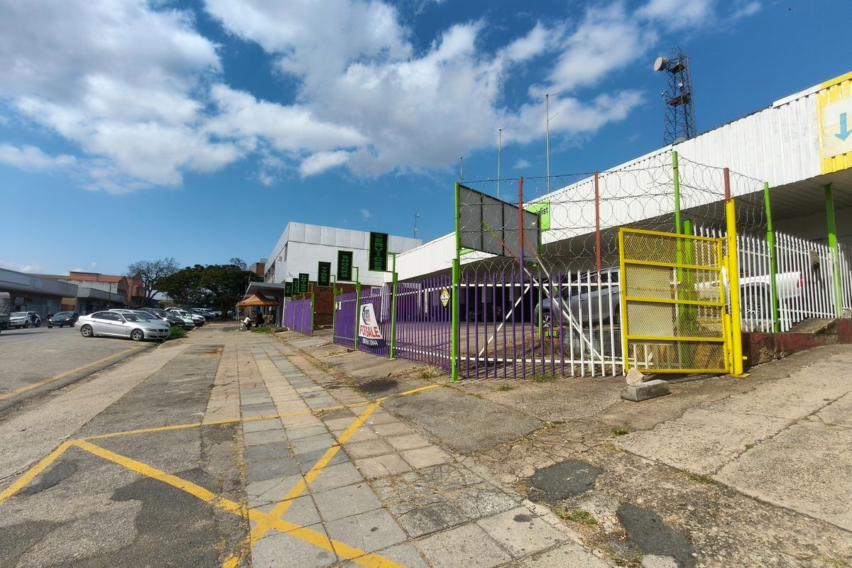 Street-level view of a commercial property featuring security fencing, razor wire, and a paved sidewalk area.