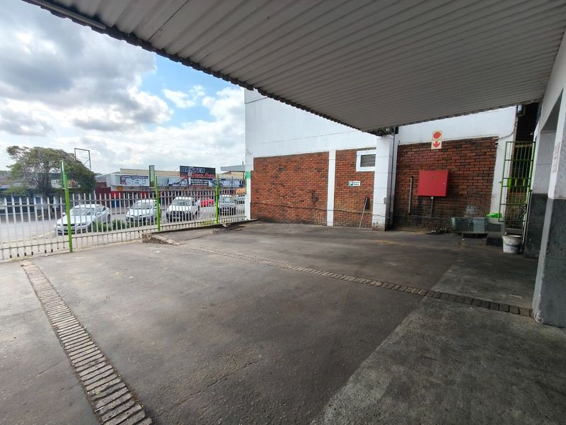 Covered parking area featuring a corrugated metal roof, brick facade, and secure metal fencing, providing functional outdoor space for the business premises.
