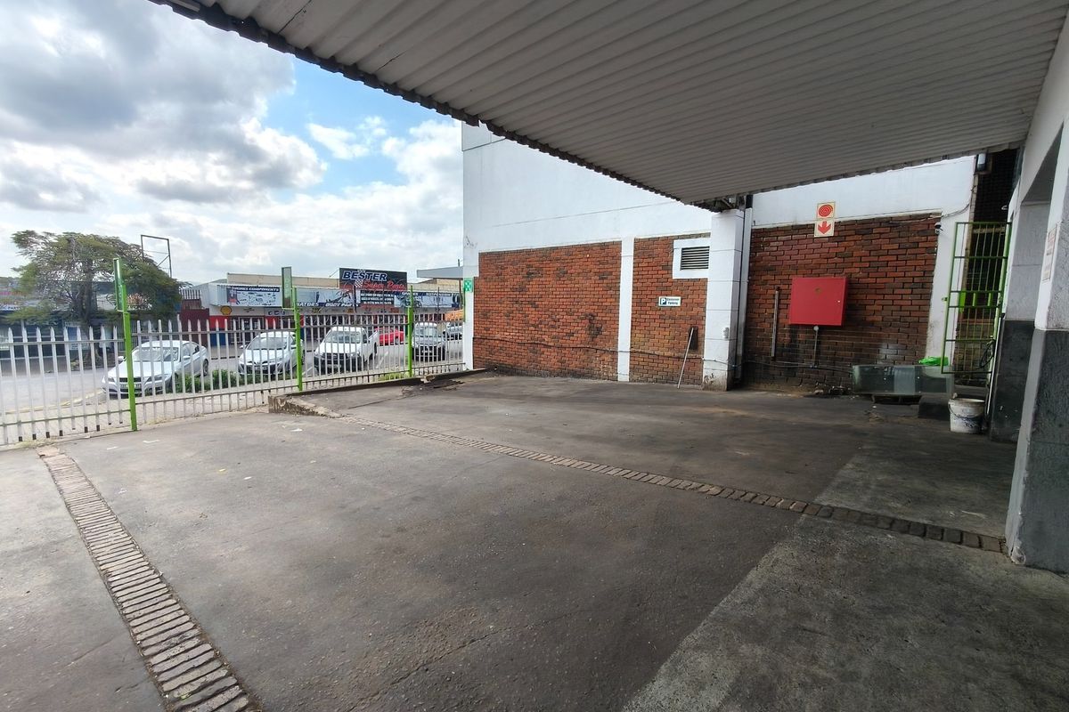 Covered parking area featuring a corrugated metal roof, brick facade, and secure metal fencing, providing functional outdoor space for the business premises.