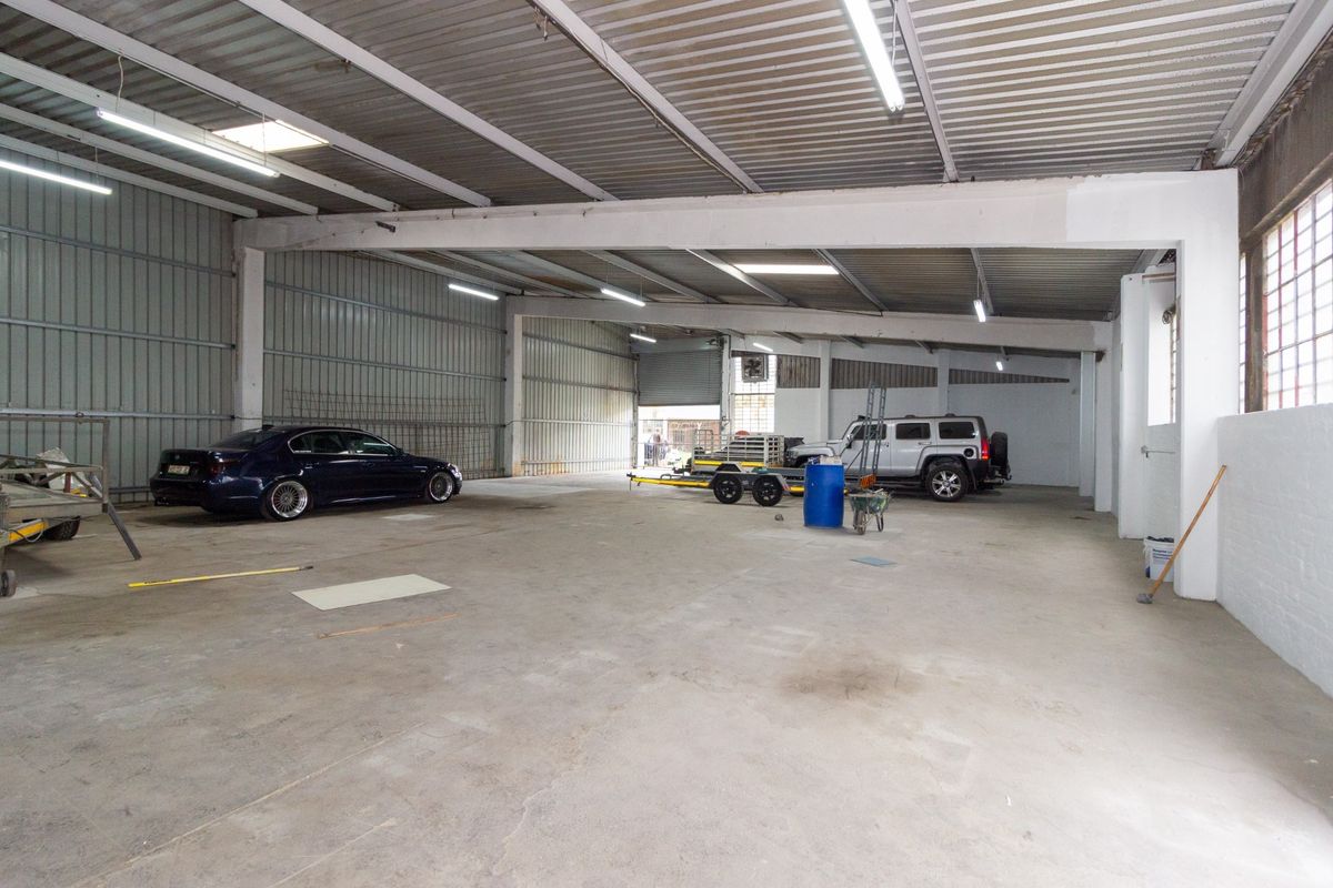 Spacious industrial garage featuring high ceilings, corrugated metal roofing, steel support beams, and durable concrete flooring, suitable for storage or workshop use.