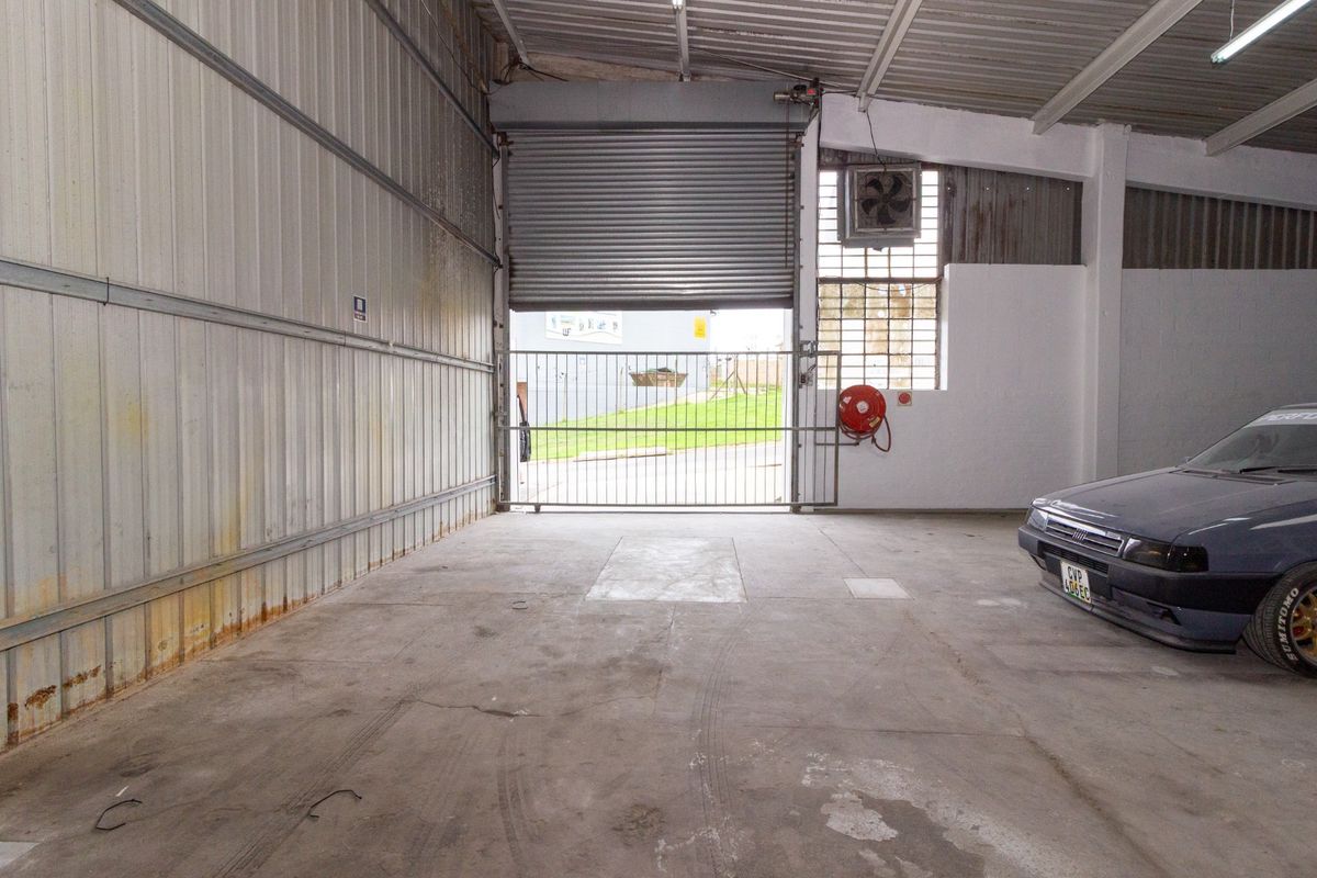 Spacious industrial garage featuring a large roller shutter door, concrete flooring, and integrated fire safety equipment, suitable for storage or workshop use.