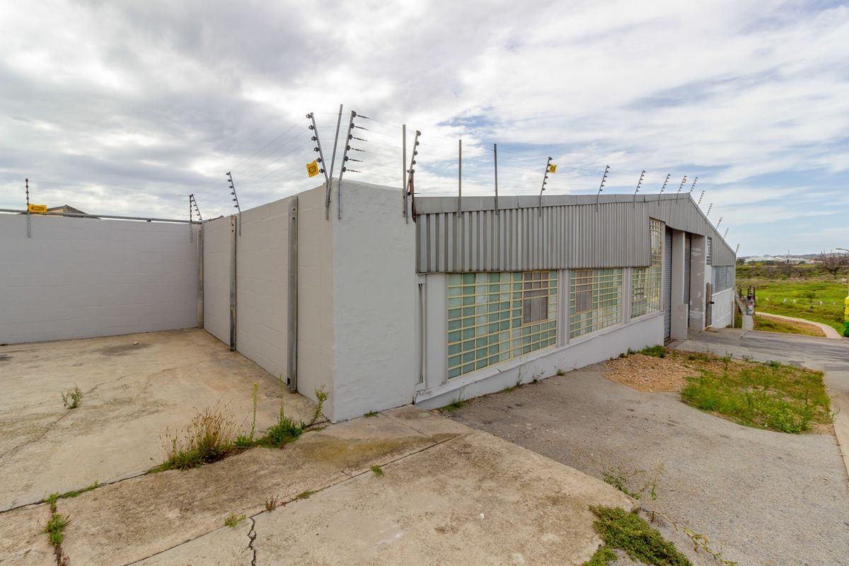 Industrial property exterior featuring concrete block walls, corrugated metal cladding, glass block windows, and perimeter electric fencing with a concrete driveway.