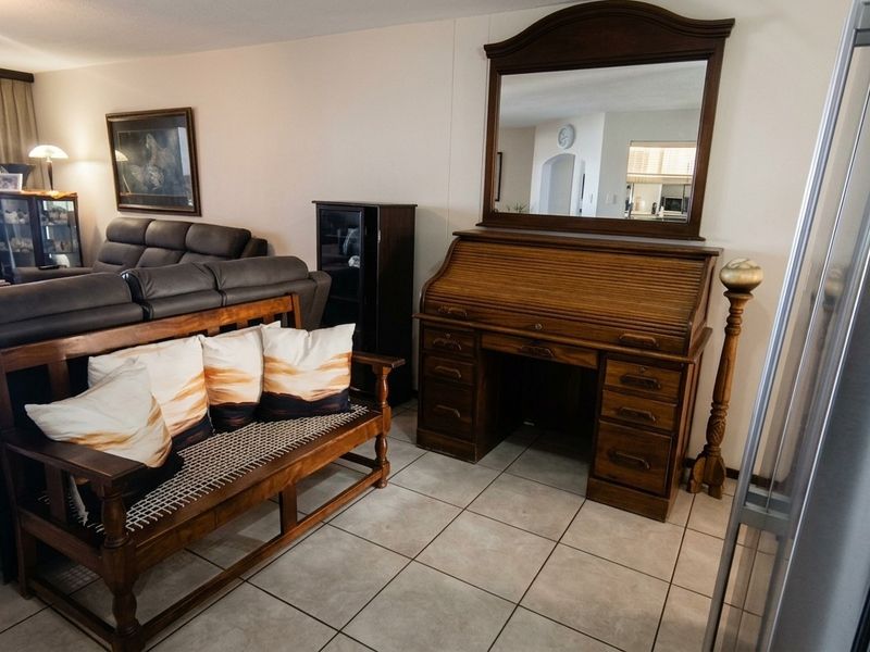 A living room area featuring neutral tiled flooring and a view into the adjacent kitchen space.