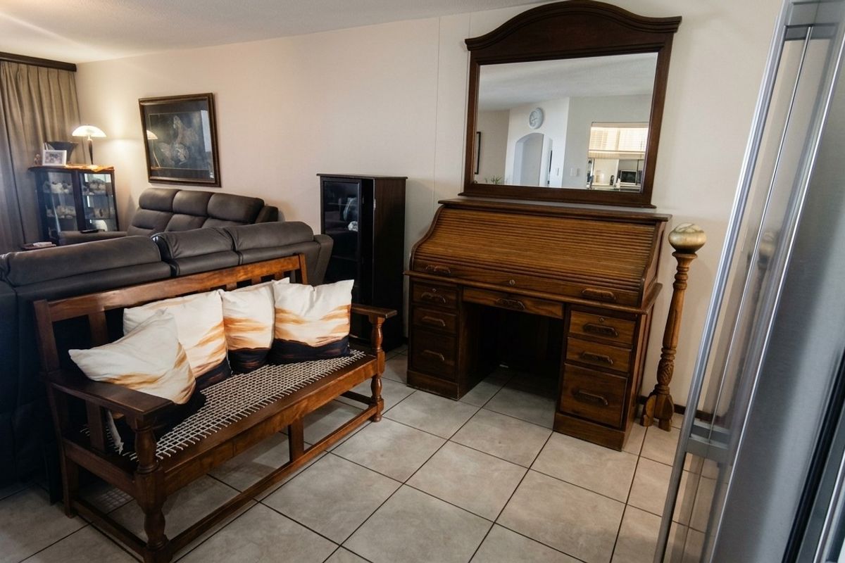 A living room area featuring neutral tiled flooring and a view into the adjacent kitchen space.
