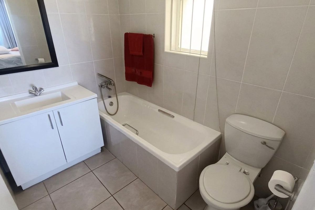 A clean, functional bathroom featuring a white vanity cabinet, integrated basin, bathtub with mixer tap, and a standard toilet with neutral wall and floor tiling.