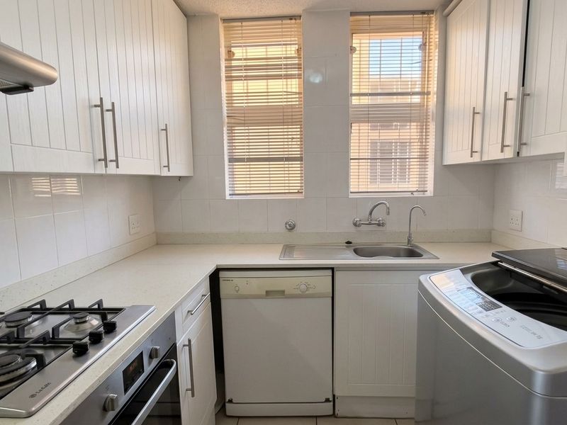 A functional kitchen featuring white cabinetry, stone countertops, a gas hob, built-in oven, and a stainless steel sink with a tiled backsplash.