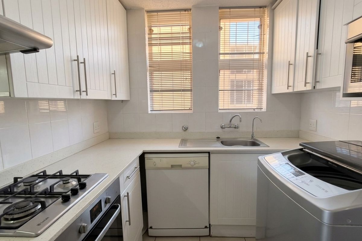 A functional kitchen featuring white cabinetry, stone countertops, a gas hob, built-in oven, and a stainless steel sink with a tiled backsplash.