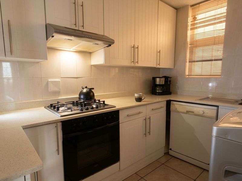 A functional kitchen featuring white cabinetry, stone countertops, a gas hob with extractor fan, and tiled finishes throughout.