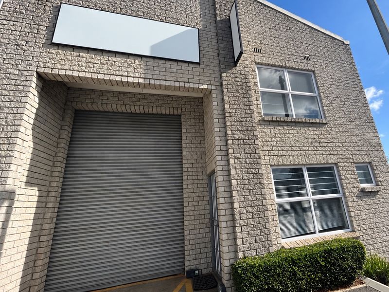 Front elevation of an industrial unit featuring a large roller shutter door, brick facade, and office windows with integrated signage space.
