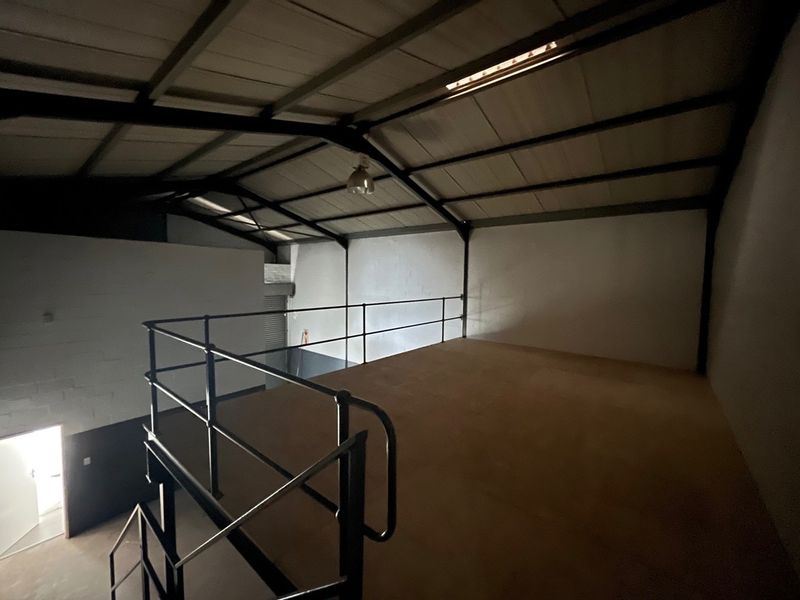 An open-plan industrial mezzanine level featuring exposed steel roof trusses, metal safety railings, and a staircase, suitable for storage or office conversion.