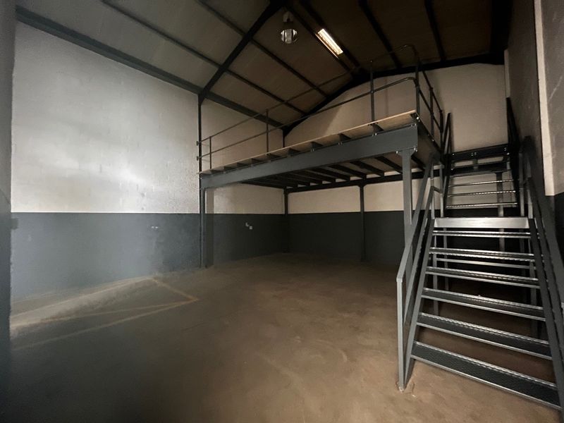 Spacious industrial utility area featuring a steel mezzanine level, metal staircase, exposed roof trusses, and durable concrete flooring.