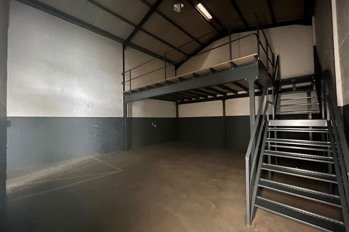 Spacious industrial utility area featuring a steel mezzanine level, metal staircase, exposed roof trusses, and durable concrete flooring.