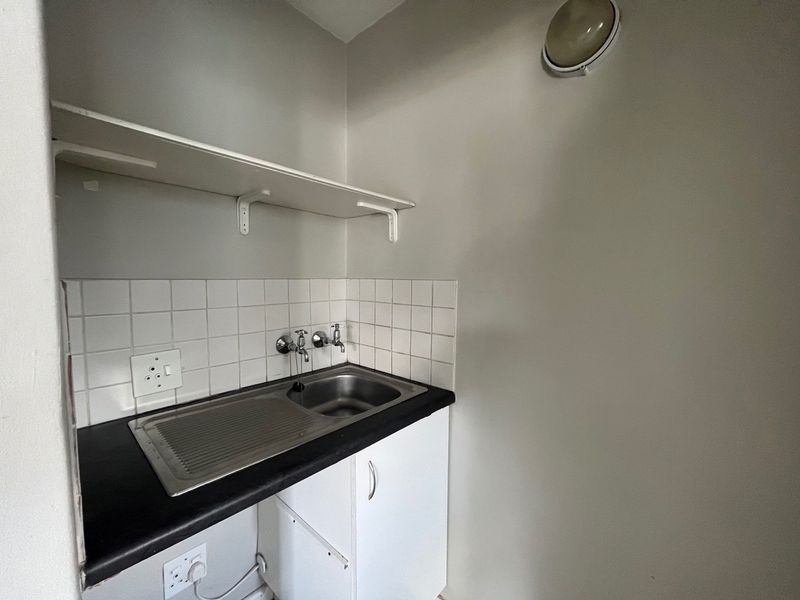 A functional laundry or utility area featuring a stainless steel sink, tiled splashback, built-in cabinetry, and a wall-mounted storage shelf.