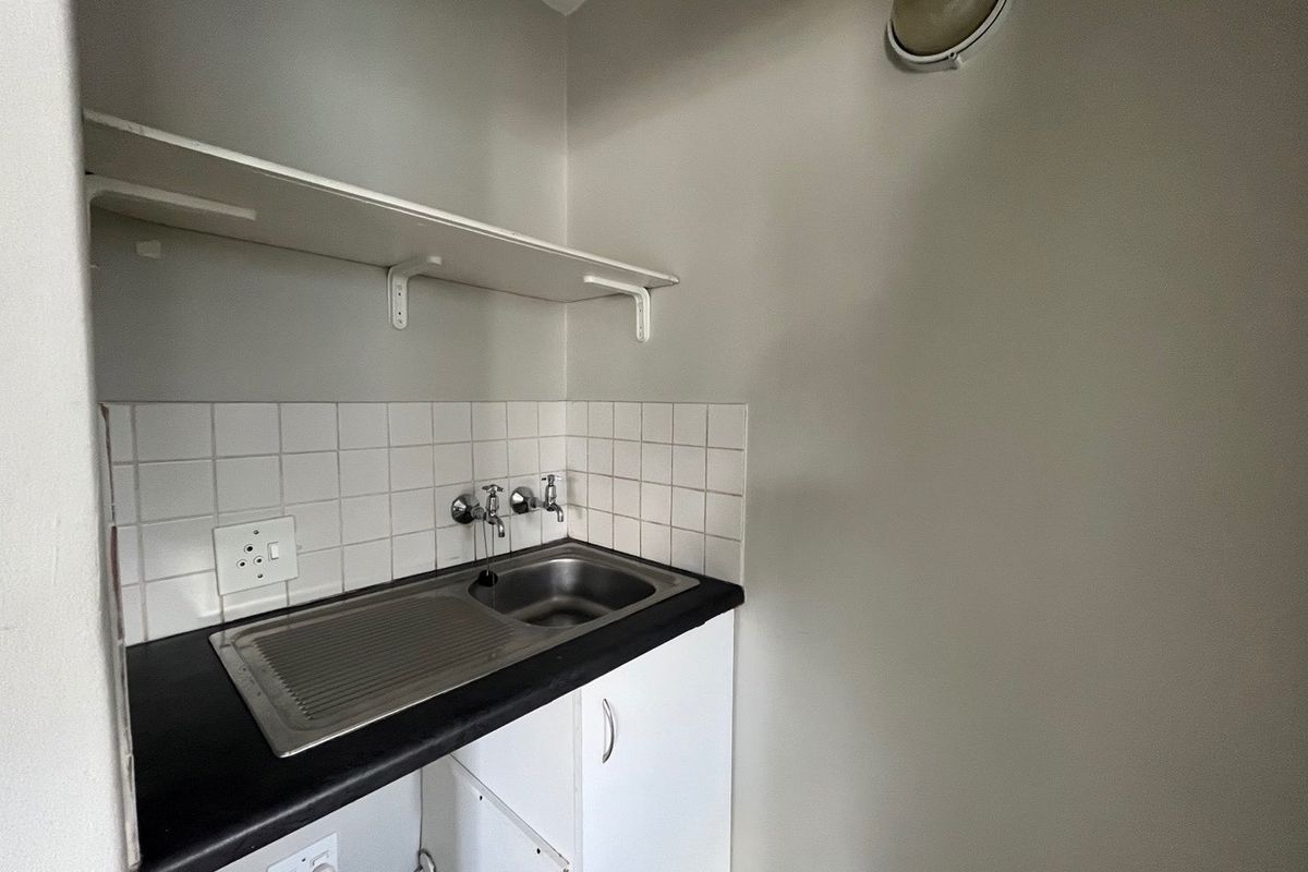 A functional laundry or utility area featuring a stainless steel sink, tiled splashback, built-in cabinetry, and a wall-mounted storage shelf.