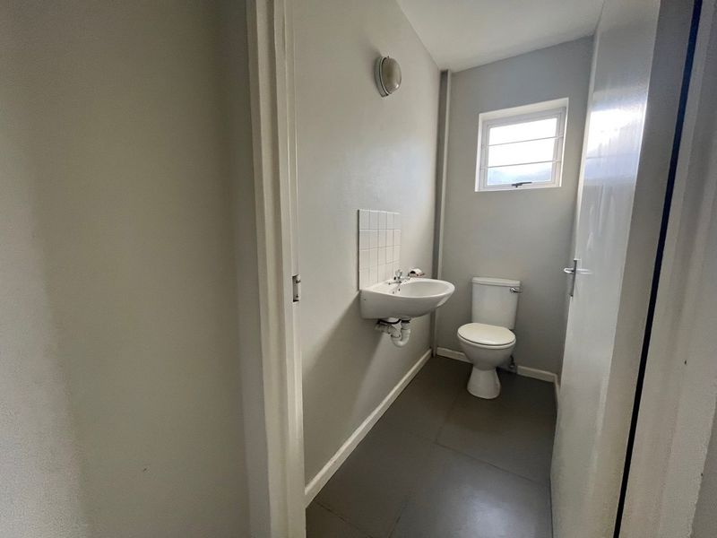A functional, compact bathroom featuring a wall-mounted basin with tiled splashback, a standard toilet, and neutral grey flooring.