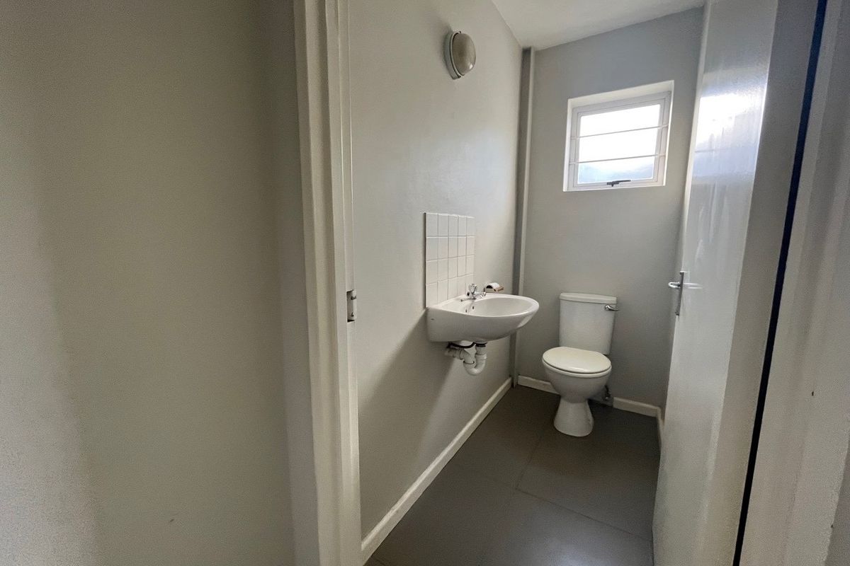 A functional, compact bathroom featuring a wall-mounted basin with tiled splashback, a standard toilet, and neutral grey flooring.