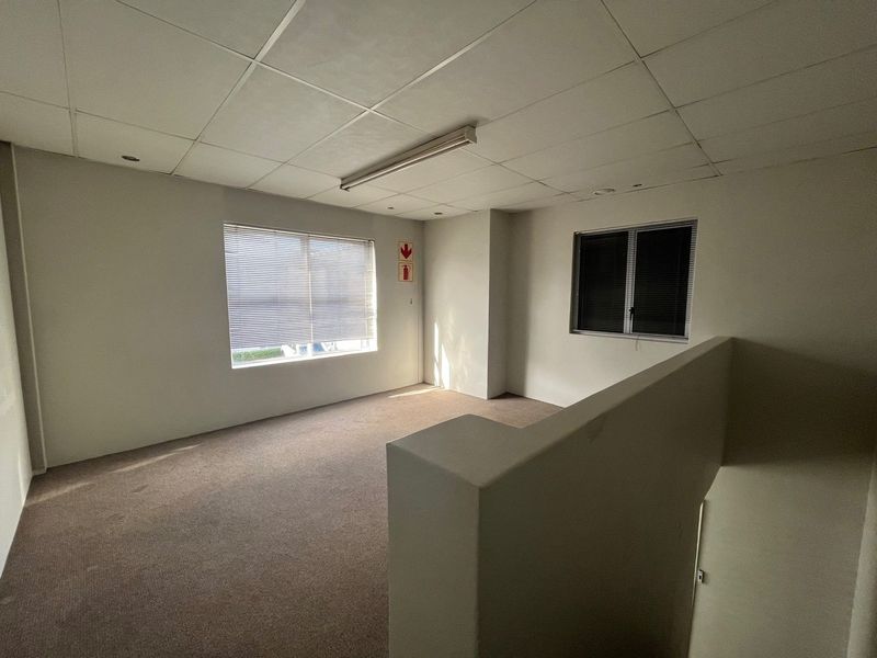 An empty office space featuring a suspended ceiling, carpeted flooring, and natural light through venetian blinds.
