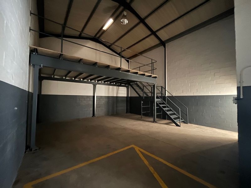 Industrial utility space featuring a mezzanine level with steel staircase, high ceilings with exposed rafters, and durable concrete flooring.