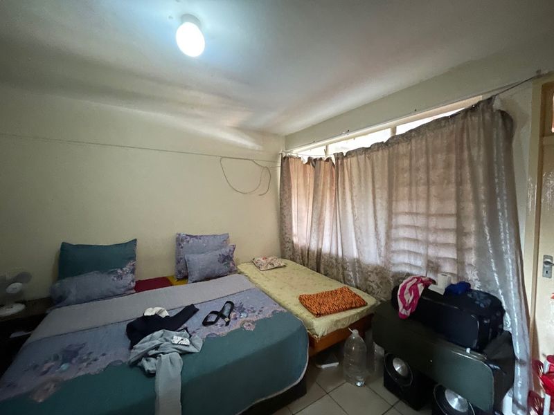 A bedroom featuring tiled flooring and a ceiling light fixture, currently requiring maintenance to address exposed wall wiring.