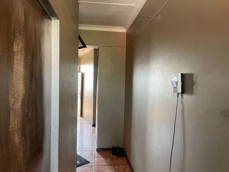 A narrow hallway featuring tiled flooring, coved ceilings, and a wall-mounted intercom system, showing signs of wear on the walls and door frames.