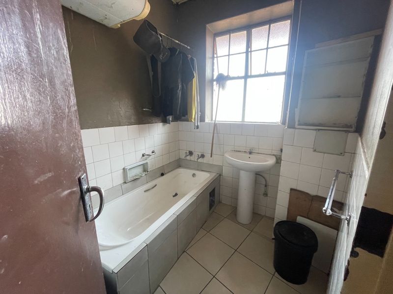 A dated bathroom featuring a built-in bathtub, pedestal basin, and tiled finishes, requiring significant renovation and modernization to improve its overall condition and appeal.