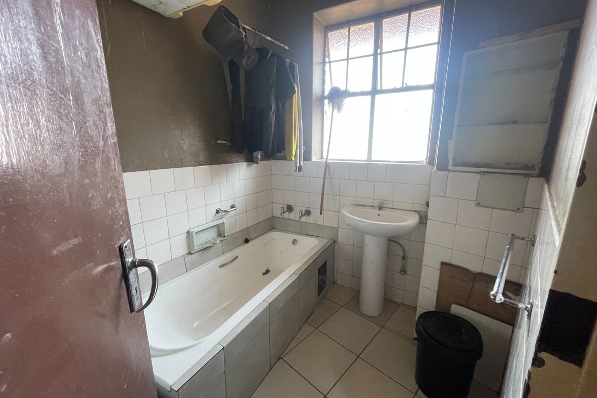 A dated bathroom featuring a built-in bathtub, pedestal basin, and tiled finishes, requiring significant renovation and modernization to improve its overall condition and appeal.