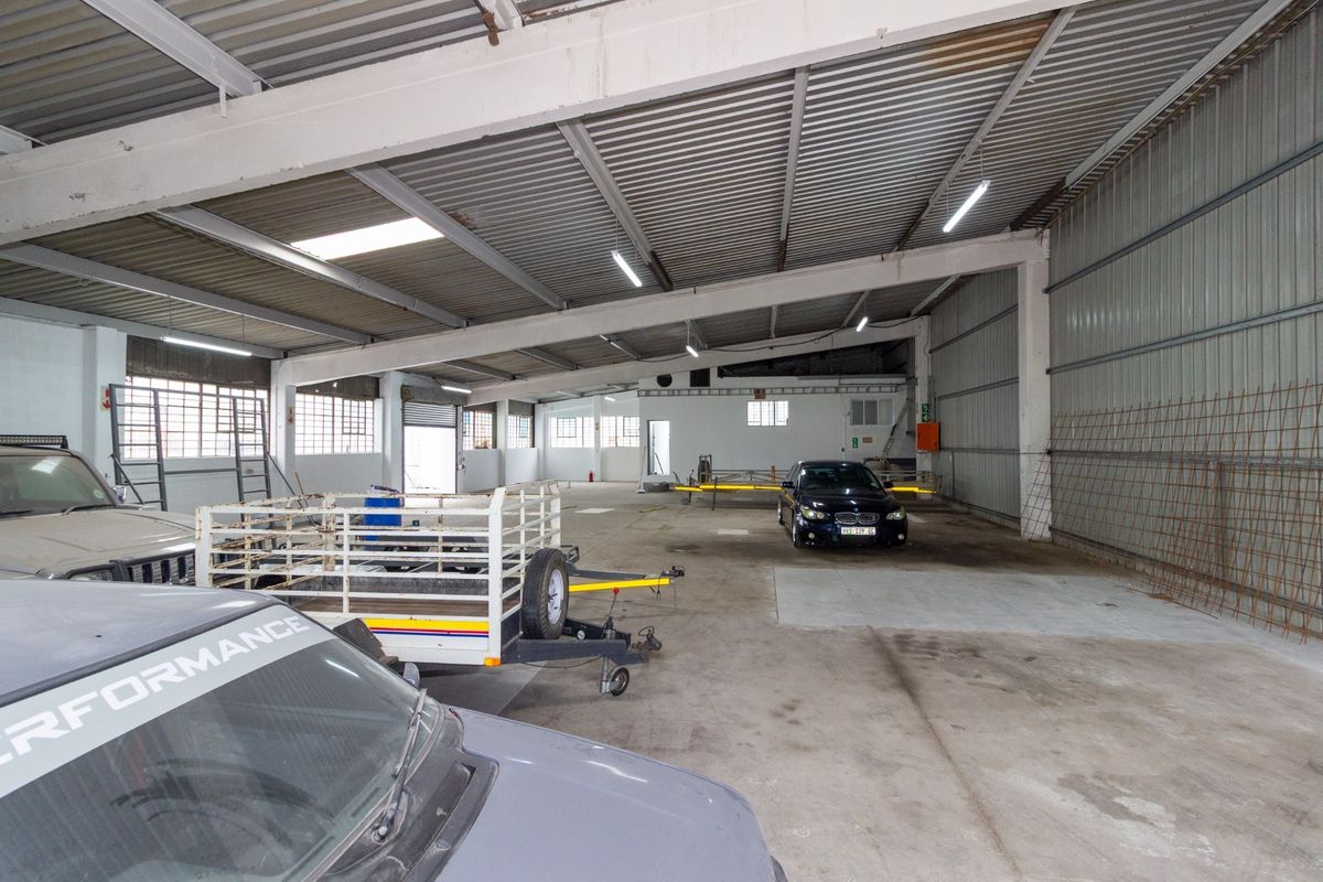 Spacious industrial garage featuring high ceilings with exposed steel beams, corrugated metal roofing, and durable concrete flooring, suitable for storage or workshop use.