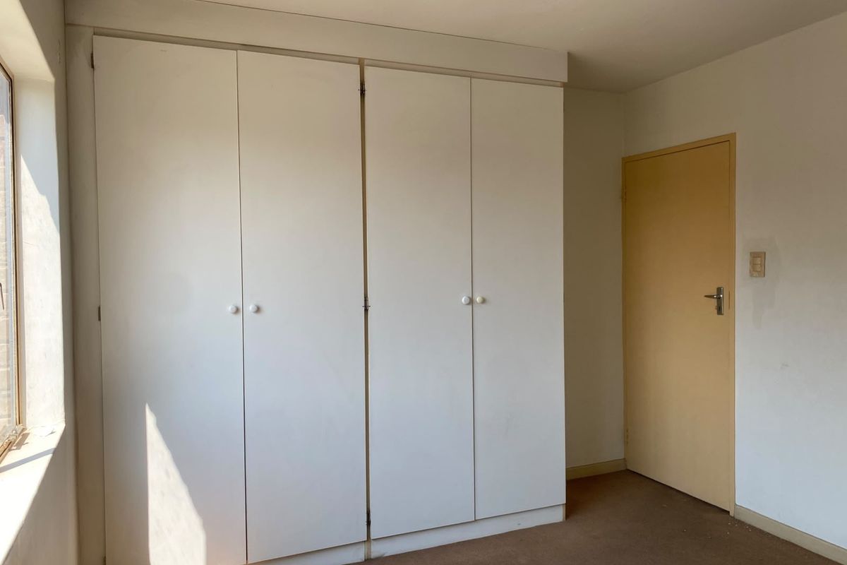 A vacant bedroom featuring built-in white cupboards, carpeted flooring, and a neutral interior door, offering a blank canvas for renovation.