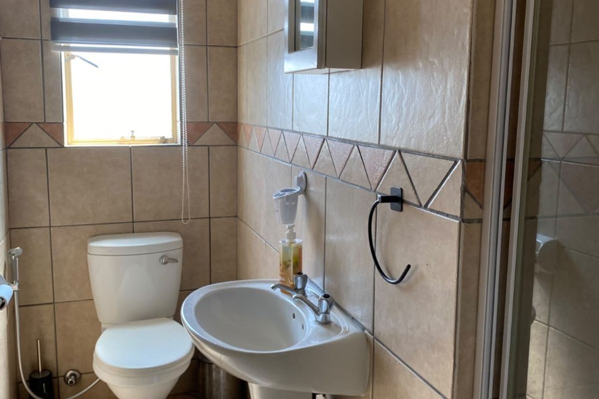 A functional bathroom featuring a pedestal washbasin, toilet, and shower enclosure with neutral wall and floor tiling.