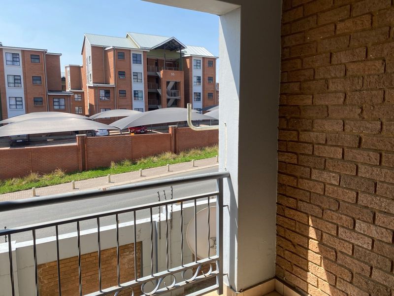 A private balcony featuring a brick feature wall, metal safety railing, and tiled flooring, overlooking the complex parking area and street.