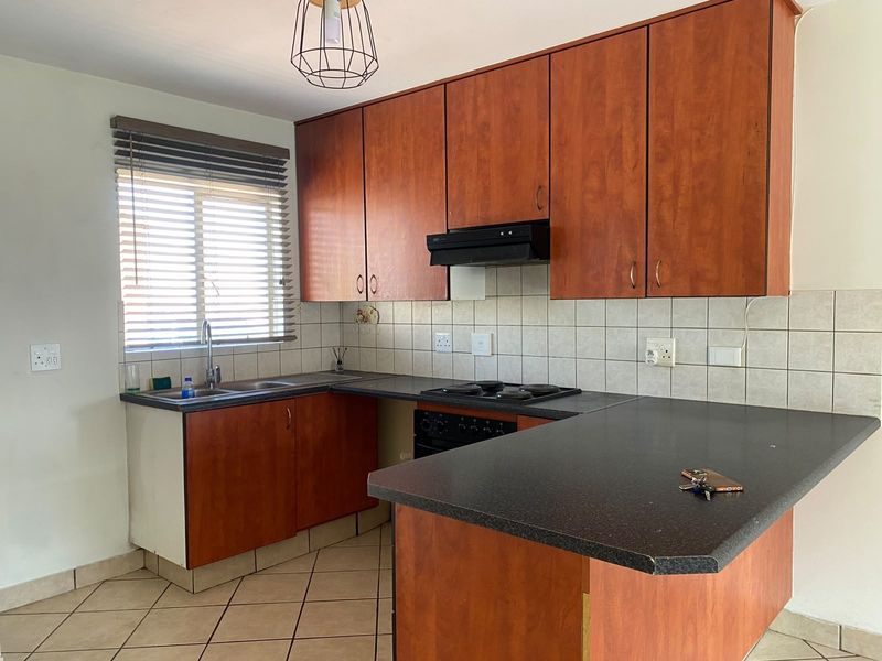A functional kitchen featuring wood-look laminate cabinetry, dark countertops, built-in oven and hob, tiled backsplash, and ceramic floor tiles.