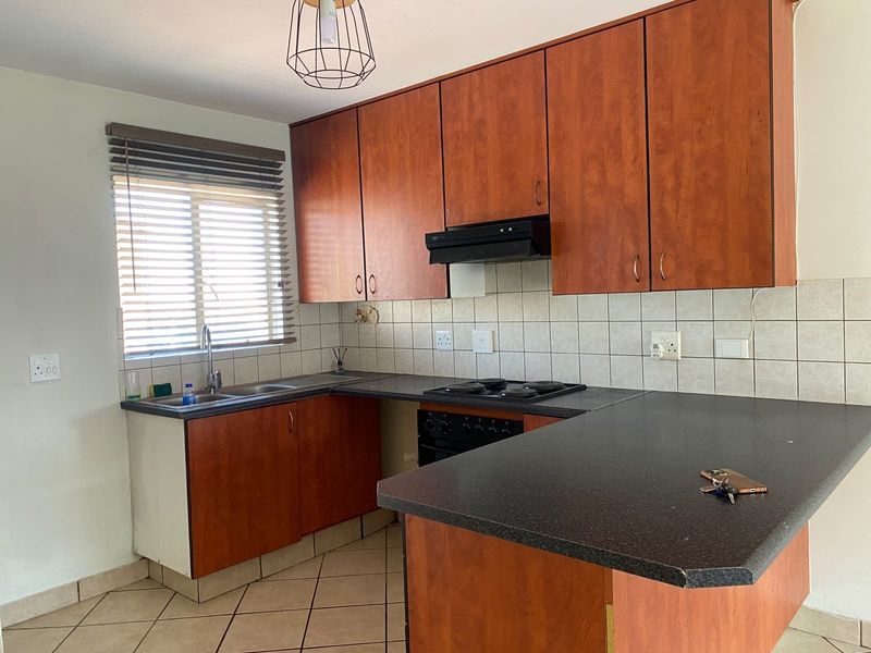A functional kitchen featuring wood-look cabinetry, dark laminate countertops, built-in oven, hob, extractor fan, and tiled flooring.