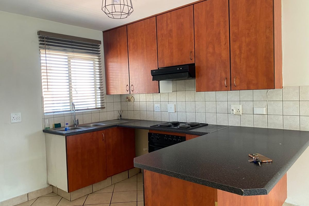 A functional kitchen featuring wood-look cabinetry, dark laminate countertops, built-in oven, hob, extractor fan, and tiled flooring.