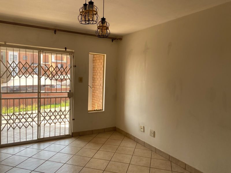 An empty living area featuring ceramic floor tiles, pendant lighting, and a security gate leading to an outdoor space, requiring minor wall maintenance.