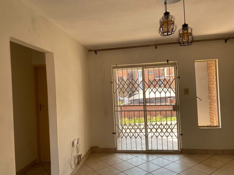 An empty living area featuring tiled floors, pendant lighting, and a security gate leading to an outdoor space, requiring minor cosmetic updates.