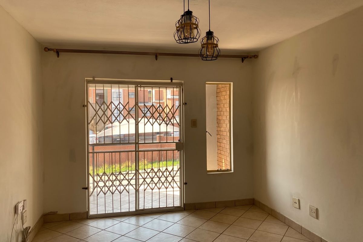 An empty living area featuring ceramic floor tiles, a sliding door with security gate, and pendant lighting, requiring minor cosmetic wall repairs.