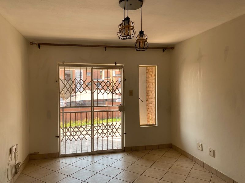An empty living area featuring ceramic floor tiles, a sliding door with security gate, and pendant lighting, requiring minor cosmetic wall repairs.