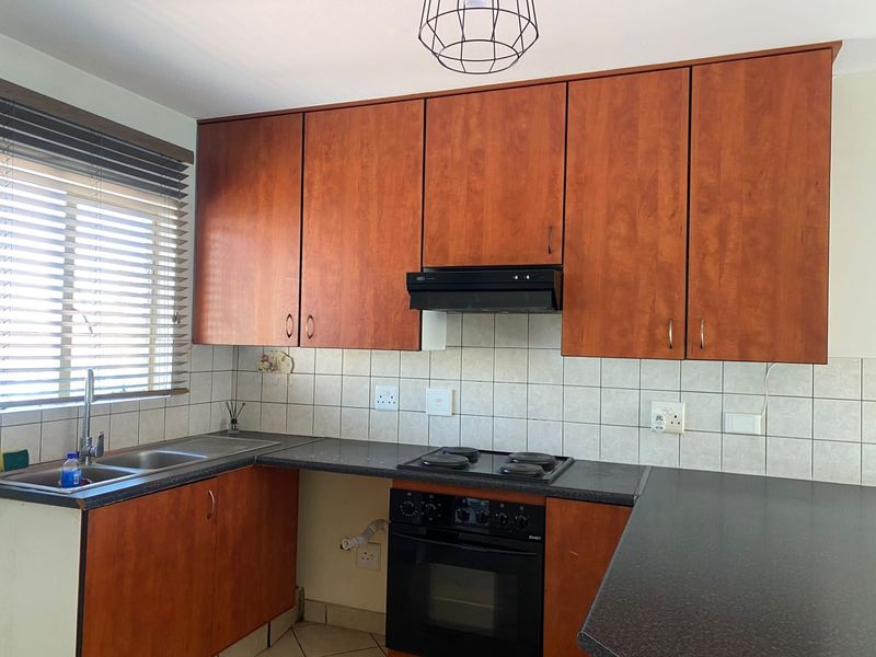 A functional kitchen featuring wooden cabinetry, dark laminate countertops, a built-in oven with hob, and a double sink with tiled backsplash.