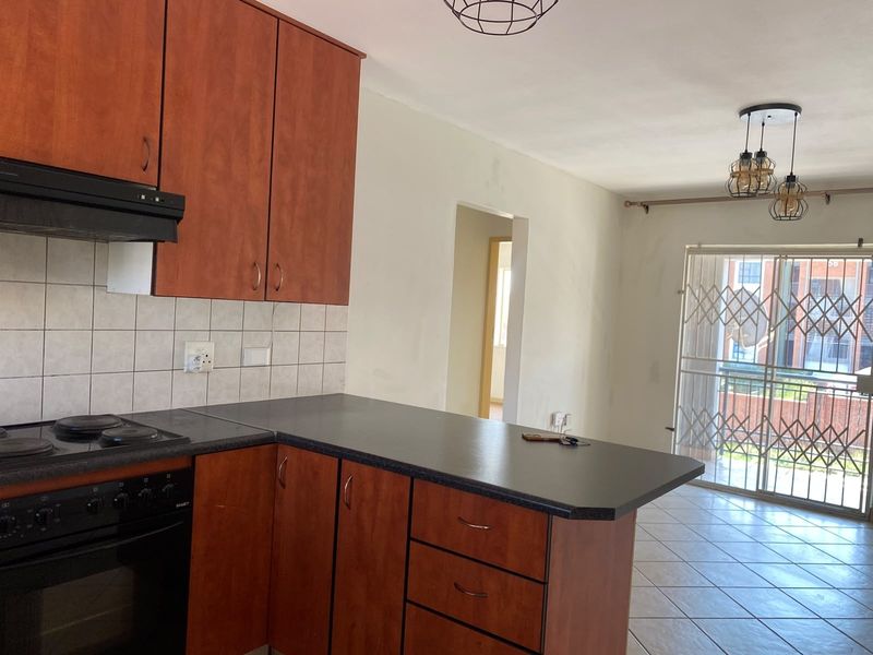Open-plan kitchen and living area featuring wood-look cabinetry, built-in appliances, and direct access to a balcony through a secure sliding door.