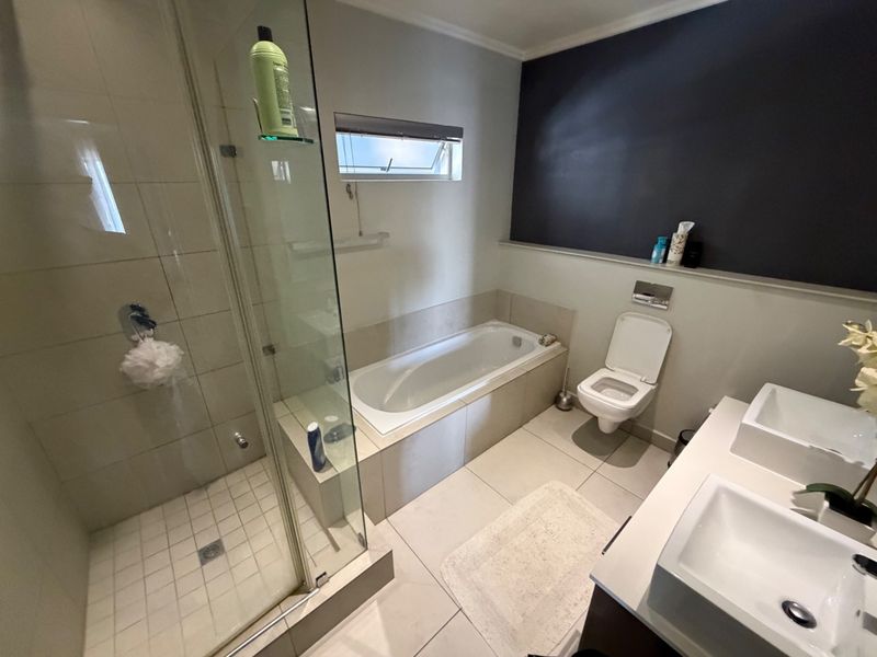 Modern bathroom featuring a glass-enclosed shower, built-in bathtub, wall-mounted toilet, and a double vanity with contemporary sinks.