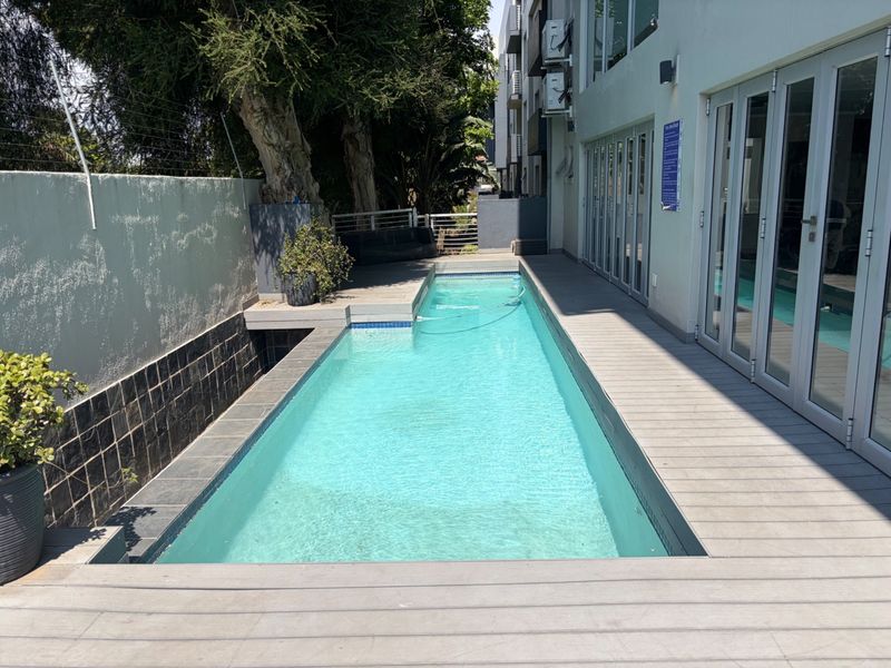 A well-maintained lap pool area featuring composite decking, glass sliding doors providing indoor-outdoor flow, and a secure boundary wall.