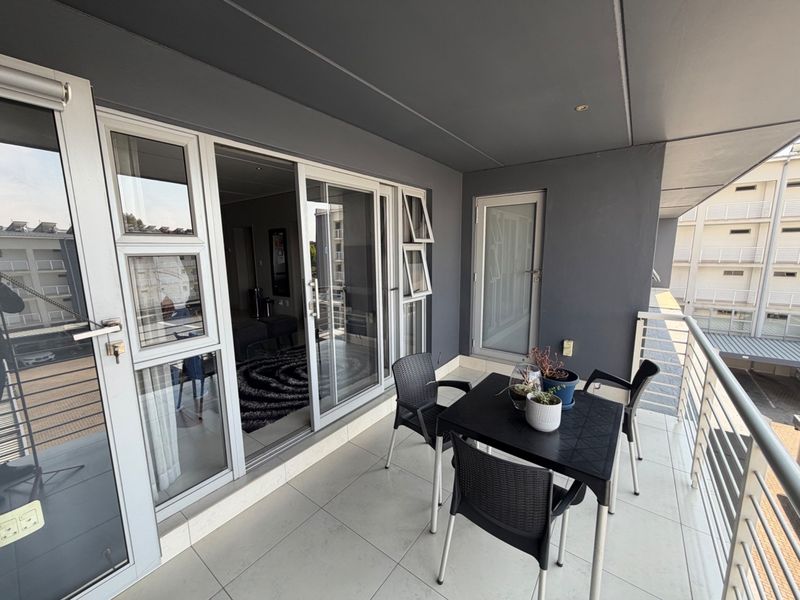 A covered balcony featuring tiled flooring, modern grey wall finishes, and sliding glass door access to the interior living space.