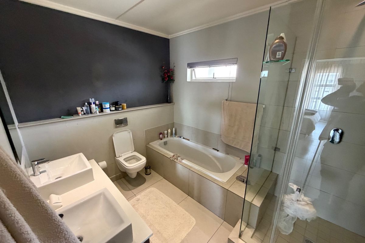 Modern bathroom featuring a double vanity, built-in bathtub, and a separate glass-enclosed shower with tiled finishes.