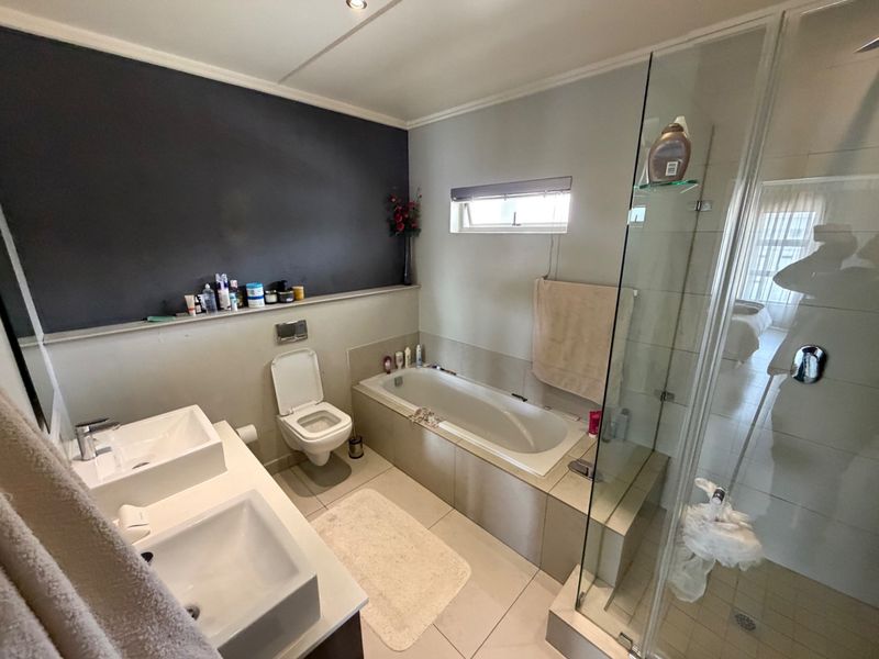 Modern bathroom featuring a double vanity, built-in bathtub, and a separate glass-enclosed shower with tiled finishes.