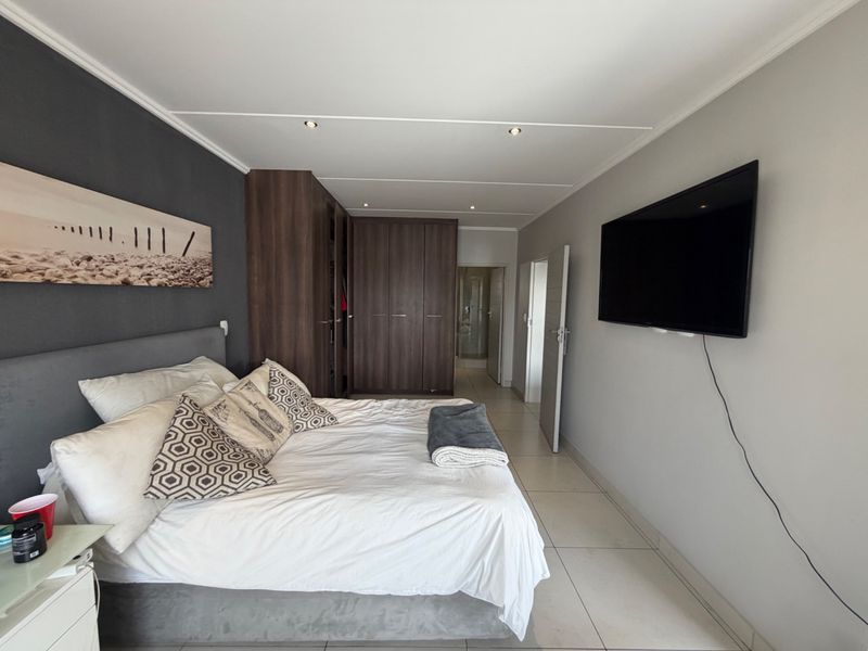 A well-maintained bedroom featuring built-in wooden cupboards, tiled flooring, recessed ceiling lighting, and direct access to an en-suite bathroom.