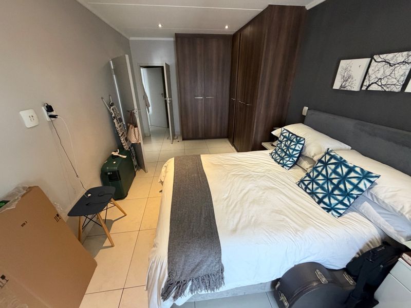 A well-maintained bedroom featuring neutral tiled flooring, dark wood built-in cupboards, and recessed ceiling lighting.