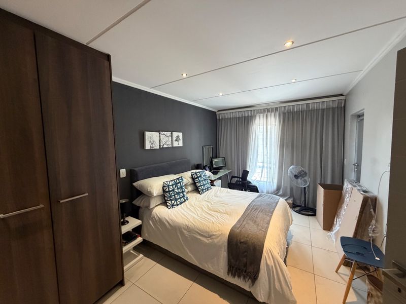 A well-maintained bedroom featuring tiled flooring, recessed downlighting, and a large built-in wardrobe with dark wood finish.