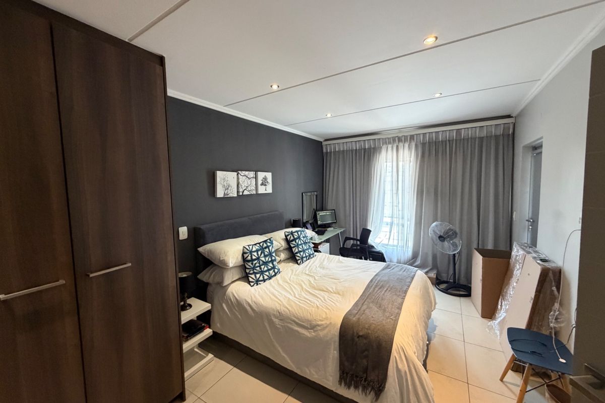 A well-maintained bedroom featuring tiled flooring, recessed downlighting, and a large built-in wardrobe with dark wood finish.